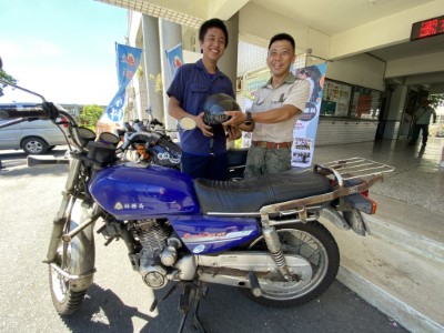 森林護管員陳俊宏參加贈車儀式，將象徵駕駛的安全帽交給汽車科學生們，表示退役的巡山機車就交由學生學習維修使用