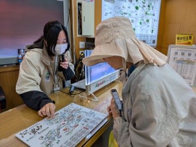 阿里山國家森林遊樂區服務人員以AI智慧櫃台輔助，向日籍遊客解說園區地圖